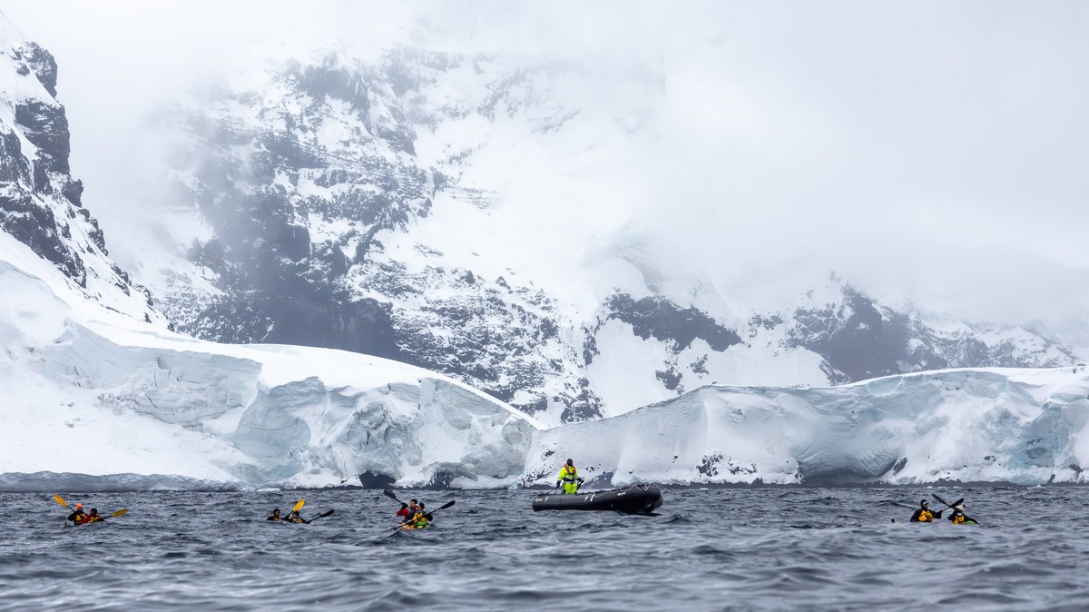 Expedition Team Kayaking in Antarctica A group of kayakers in bright yellow and red outfits explore icy Antarctic waters near massive