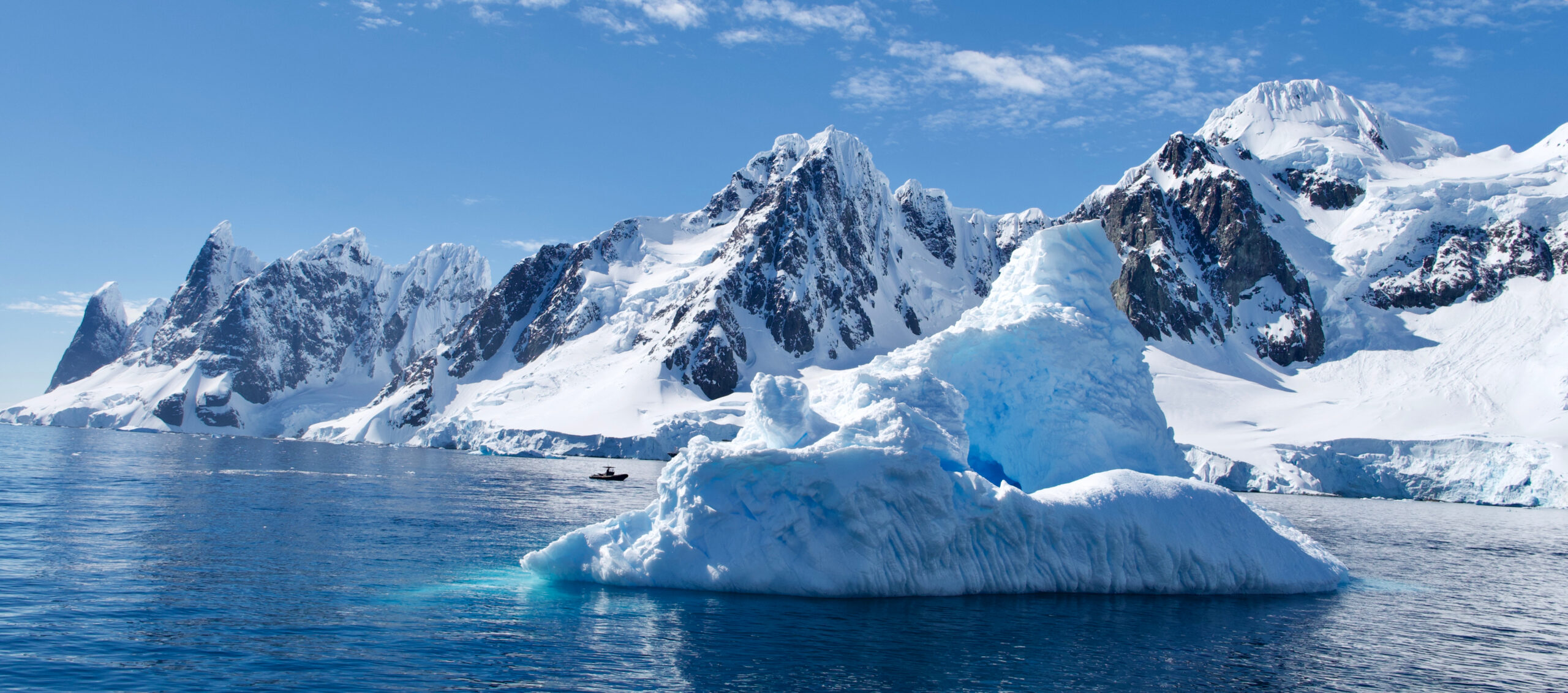 Icebergs and Snow-Capped Mountains in Antarctica A stunning Antarctic seascape featuring a large blue-and-white iceberg in the foreground floating