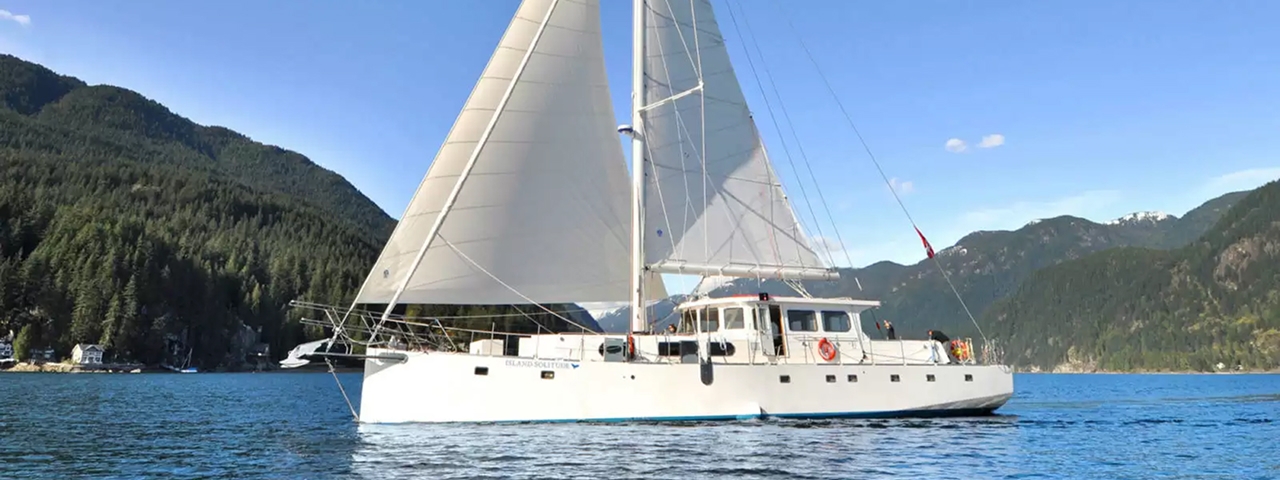 SV Island Solitude Catamaran in Mountain Lake A white sailing catamaran with full sails deployed, anchored in a pristine alpine lake surrounded