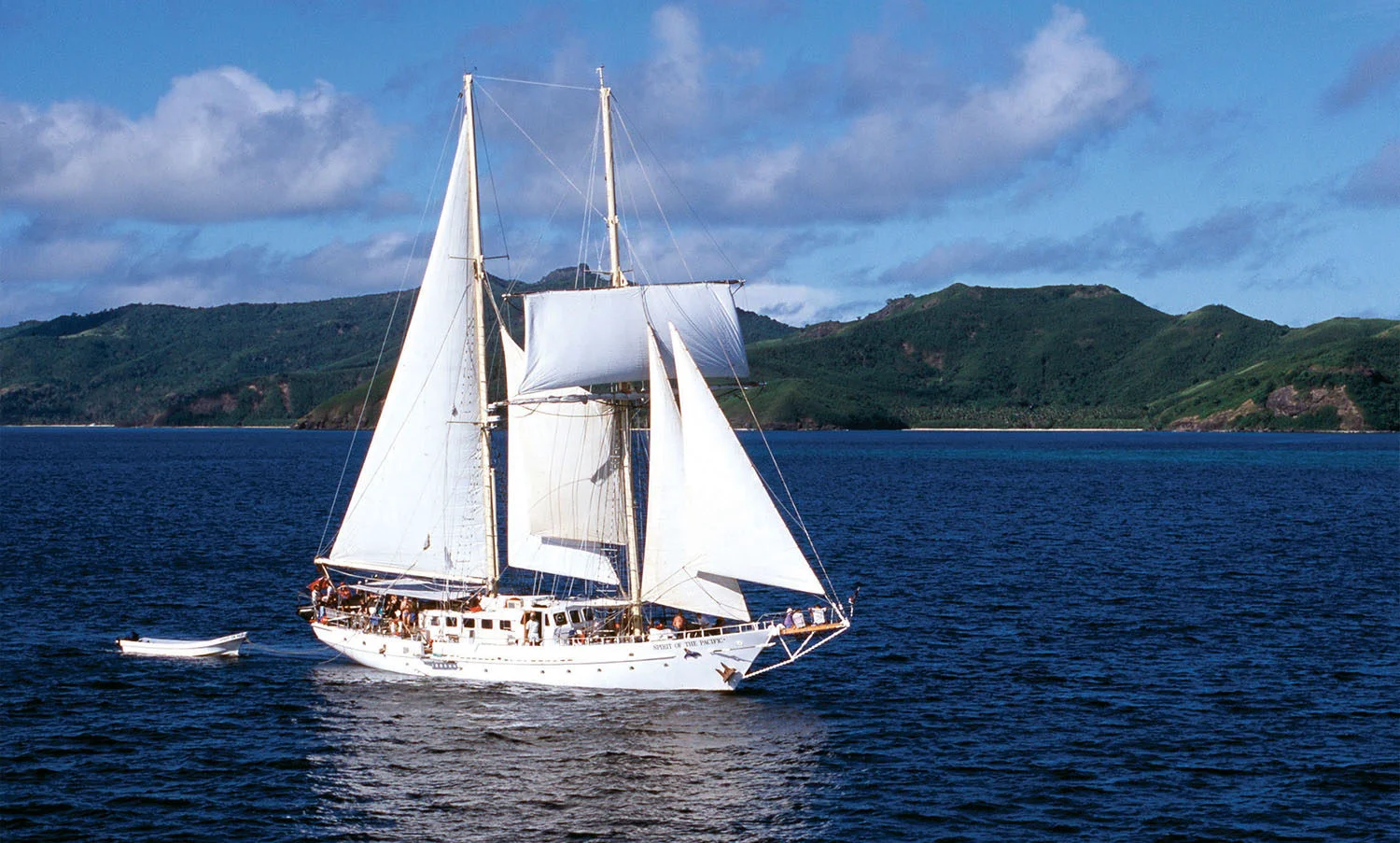 Classic Sailing Vessel in Tropical Waters A striking white-hulled sailing ship with two tall masts and full white sails anchored
