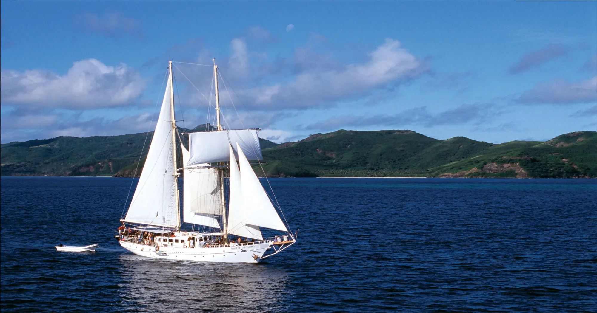 Classic Tall Ship Under Full Sail A stunning white-sailed tall ship with traditional rigging anchors in clear blue waters, with lush