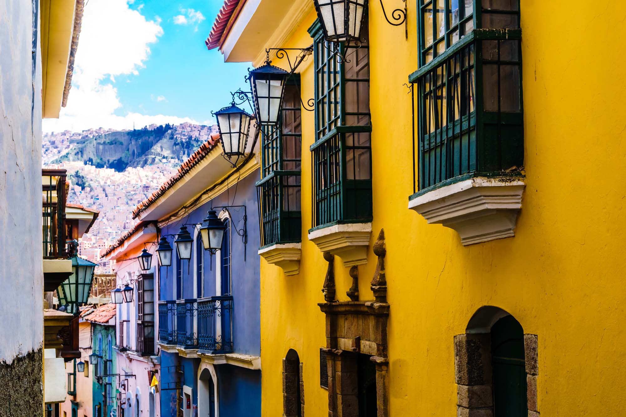 Colorful Colonial Street in La Paz, Bolivia A vibrant street scene showcasing colonial architecture with bright yellow and blue buildings, ornate balconies, and traditional street lamps, set against a mountainous backdrop.