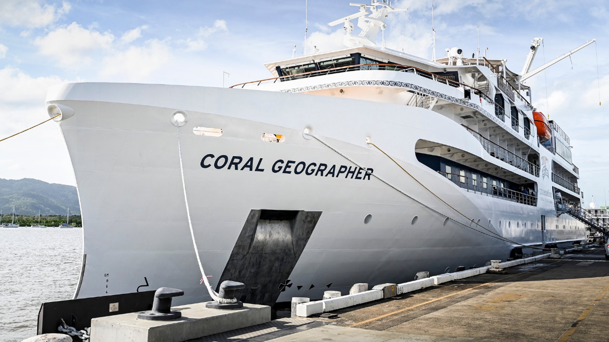 The expedition cruise ship Coral Geographer is docked at a tropical port, showcasing its white hull