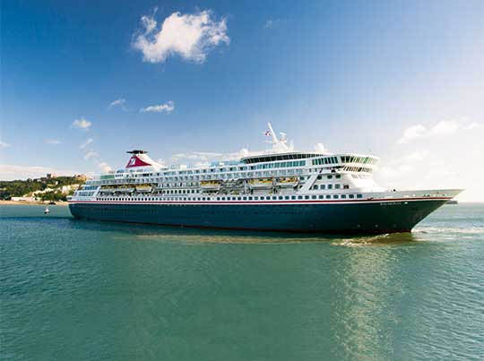A large modern cruise ship with distinctive white and dark hull livery anchored in clear turquoise