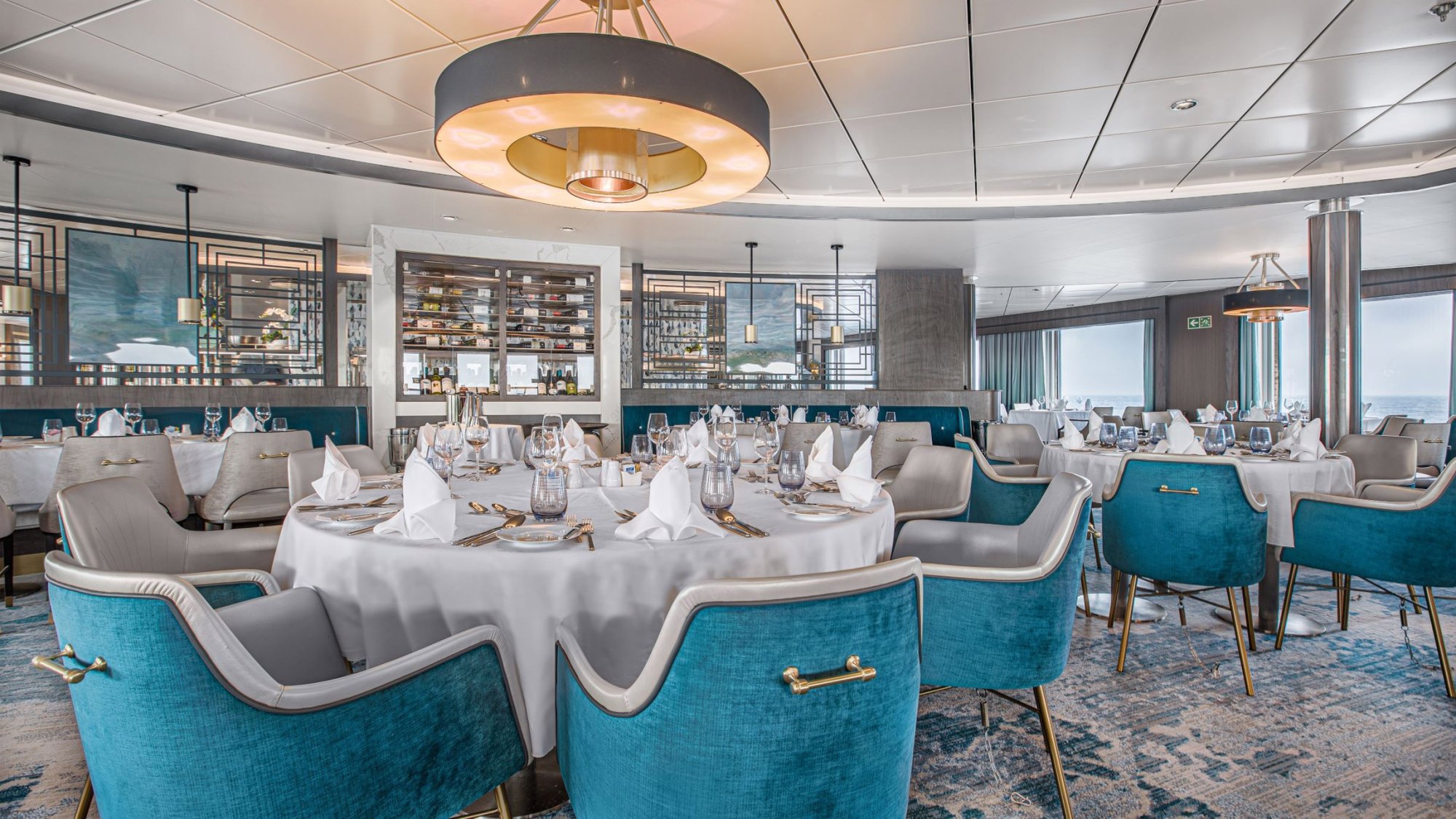 Elegant Fine Dining Restaurant Aboard Ocean Victory An upscale dining venue featuring round tables with white linens, turquoise and grey modern chairs