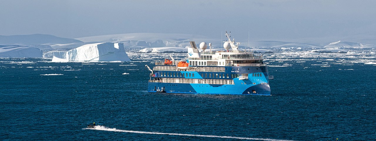 Expedition Cruise Ship with Iceberg in Arctic Waters A modern blue and white expedition cruise ship navigates Arctic waters with a large tabular iceberg
