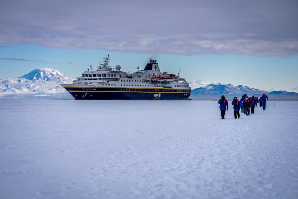 Expedition Cruise Ship on Antarctic Ice A modern expedition cruise ship anchored in pack ice with snow-covered volcanic mountains in