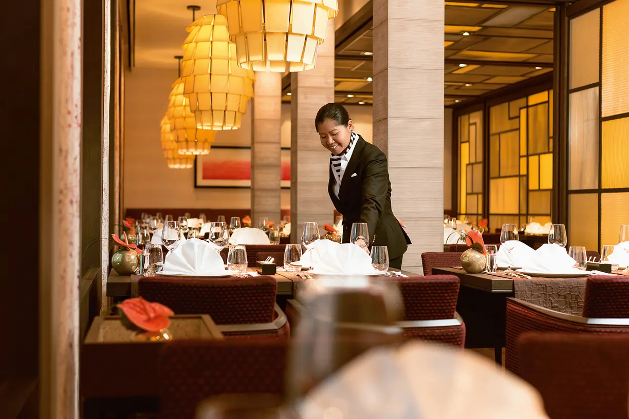 Elegant Fine Dining Service Aboard Europa 2 A professionally dressed server prepares an upscale dining table in a sophisticated restaurant