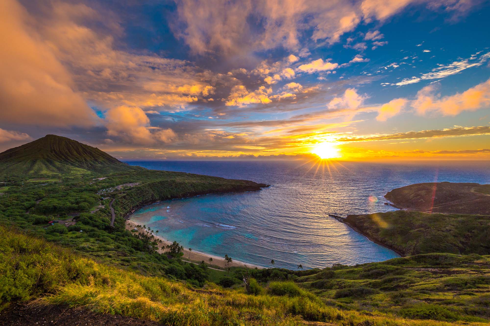 Hanauma Bay Sunrise, Hawaii A breathtaking sunrise over Hanauma Bay, showcasing a crescent-shaped turquoise bay nestled between lush green volcanic hills, with dramatic golden clouds and sunlight reflecting on the ocean.