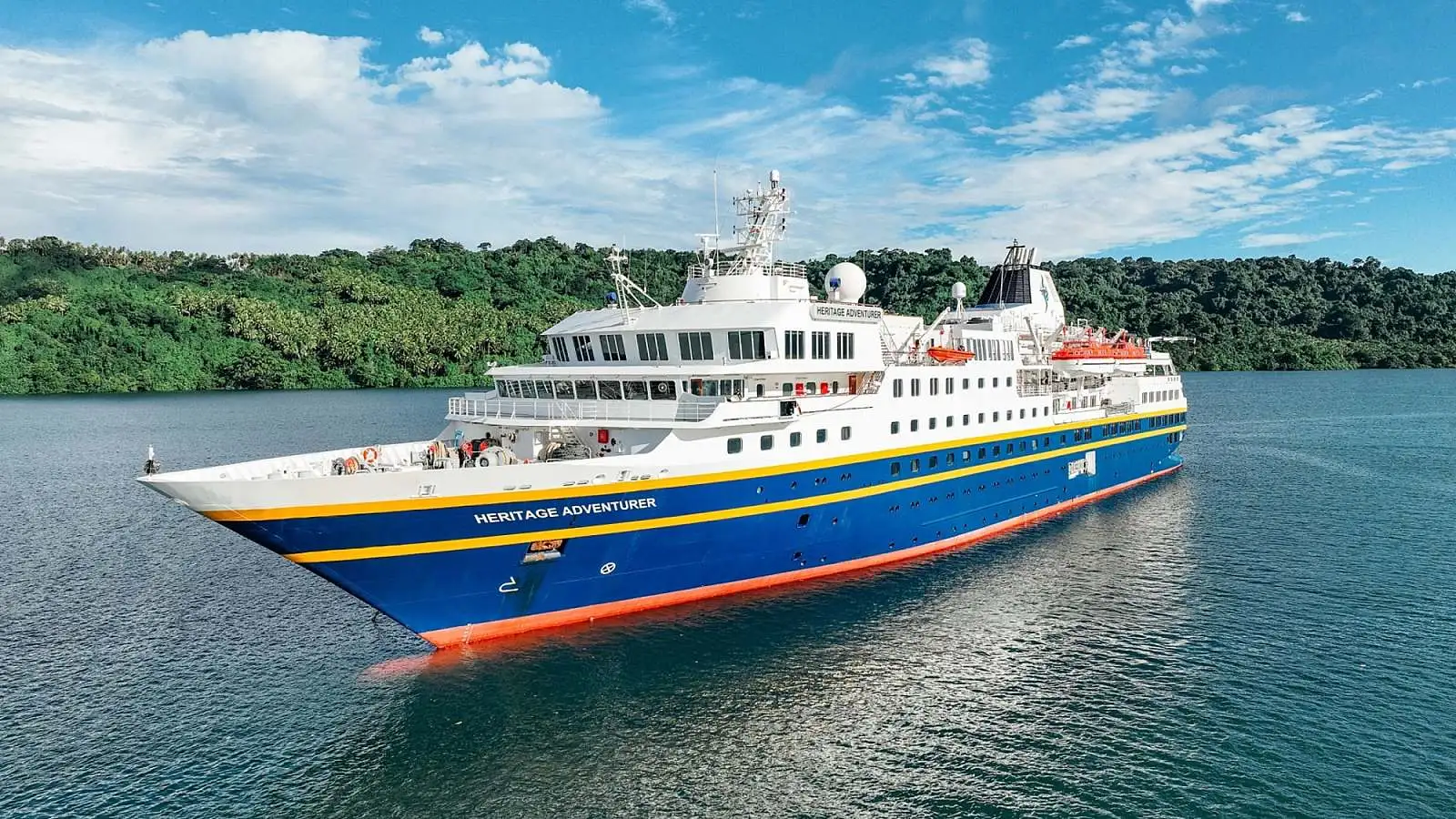 Heritage Adventurer Cruise Ship in Tropical Waters A small expedition-style cruise ship named Heritage Adventurer sailing near a lush green forested