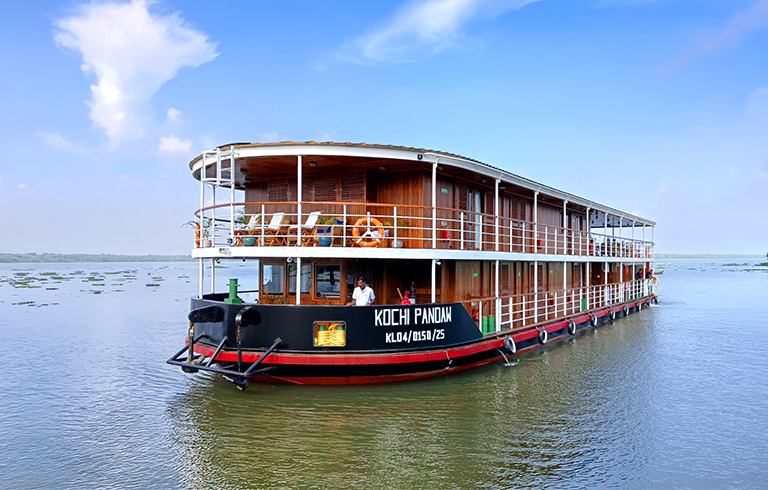 Kochi Pandan River Cruise Boat A multi-level wooden river boat named Kochi Pandan floating on calm waters with a blue sky