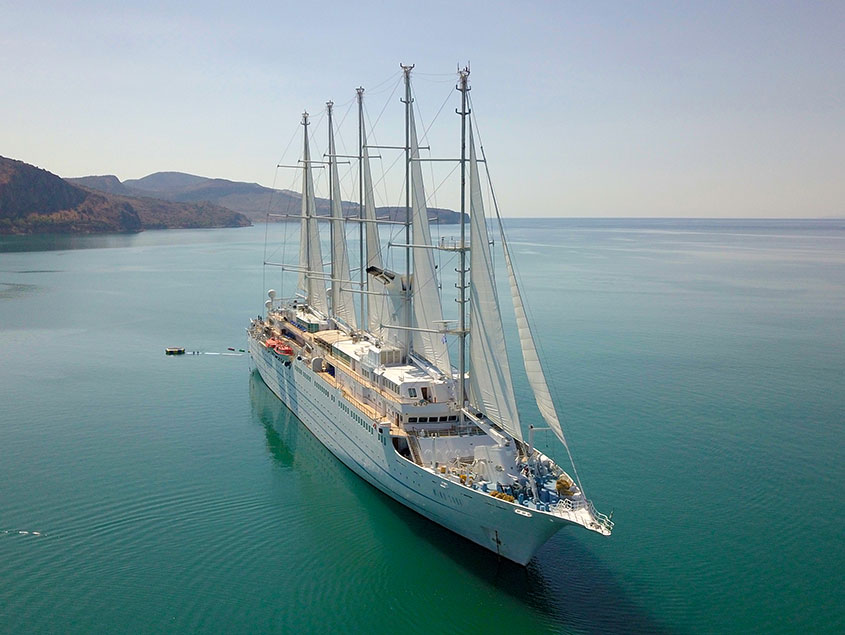 Luxurious Sailing Yacht in Calm Turquoise Waters A multi-masted sailing vessel anchored in tranquil blue-green waters with mountainous coastline
