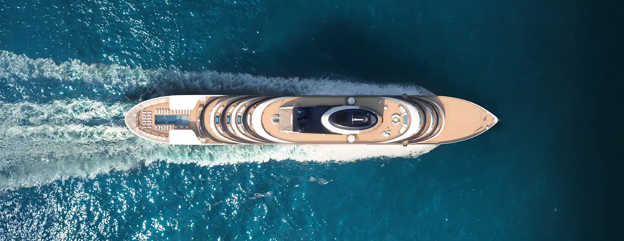 An overhead aerial view of a sleek, modern luxury expedition yacht cutting through deep turquoise