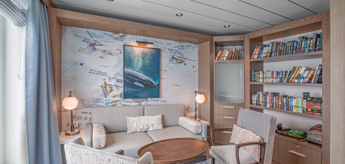 Luxury Cruise Ship Cabin with Map Wall Art A contemporary cruise ship cabin featuring twin beds with cream-colored bedding, purple and coral accent pillows, and a neutral color palette. The room showcases modern furnishings including a padded headboard, ambient lighting, and upscale décor typical of premium cruise line accommodations.