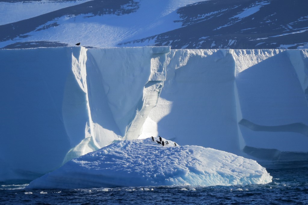 Expedition Team Exploring Antarctic Iceberg A breathtaking view of a massive Antarctic iceberg with towering white ice cliffs rising