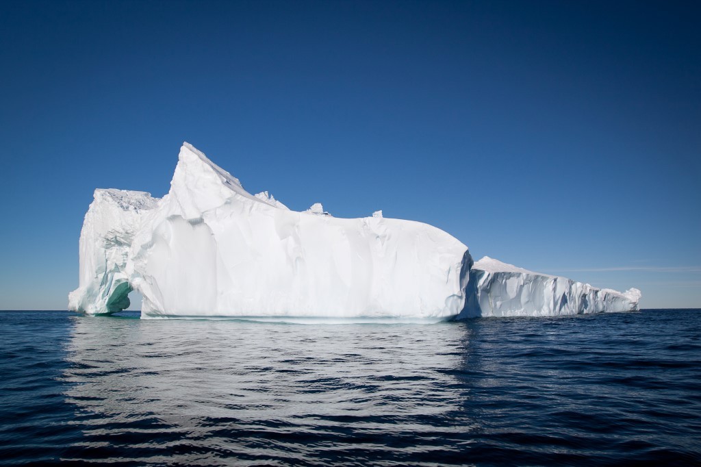 Massive Tabular Iceberg in Arctic Waters A large, brilliantly white tabular iceberg floats in deep blue Arctic ocean waters under a clear