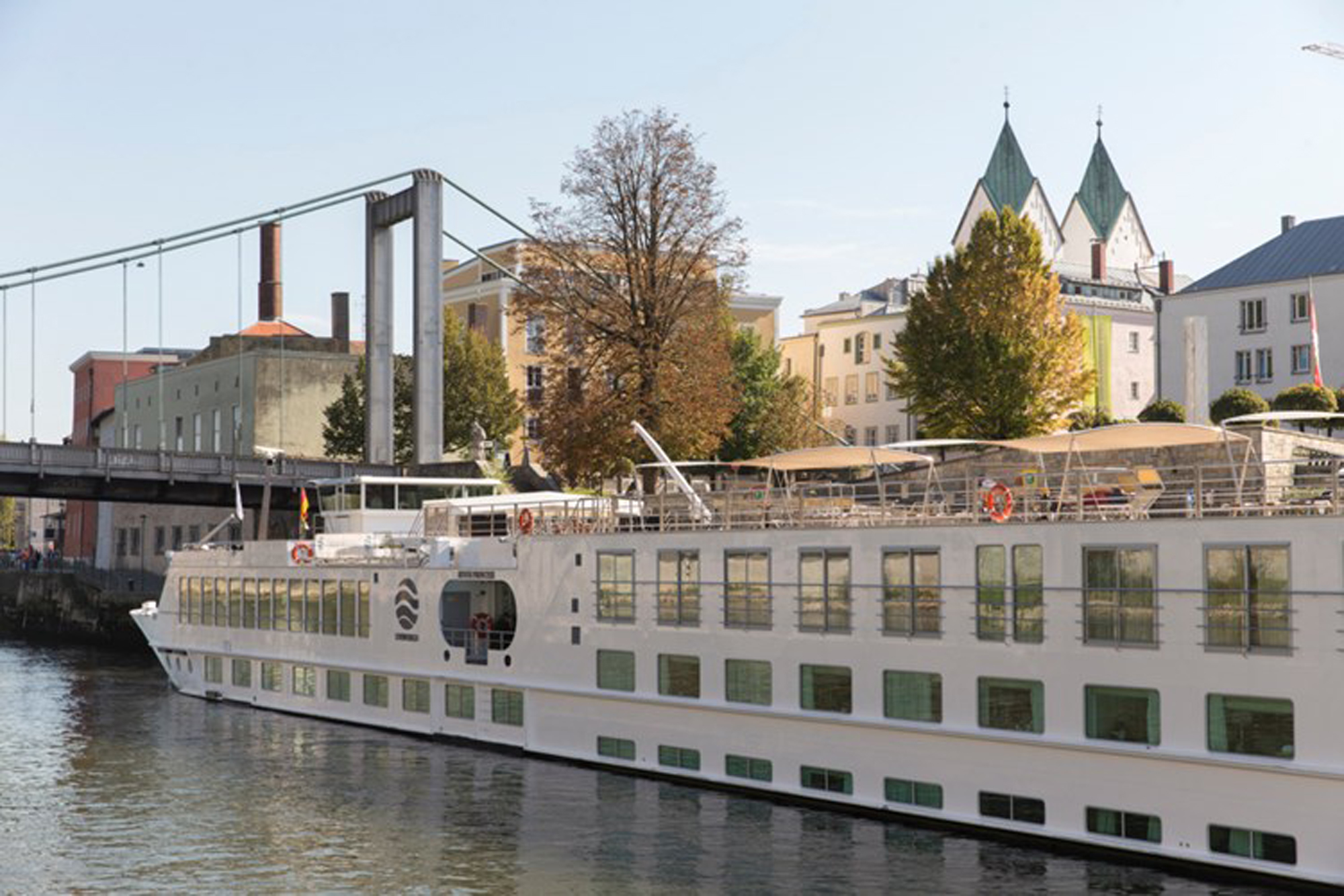 River Cruise Ship Docked in European City A modern river cruise ship with white hull and multiple passenger decks is moored alongside