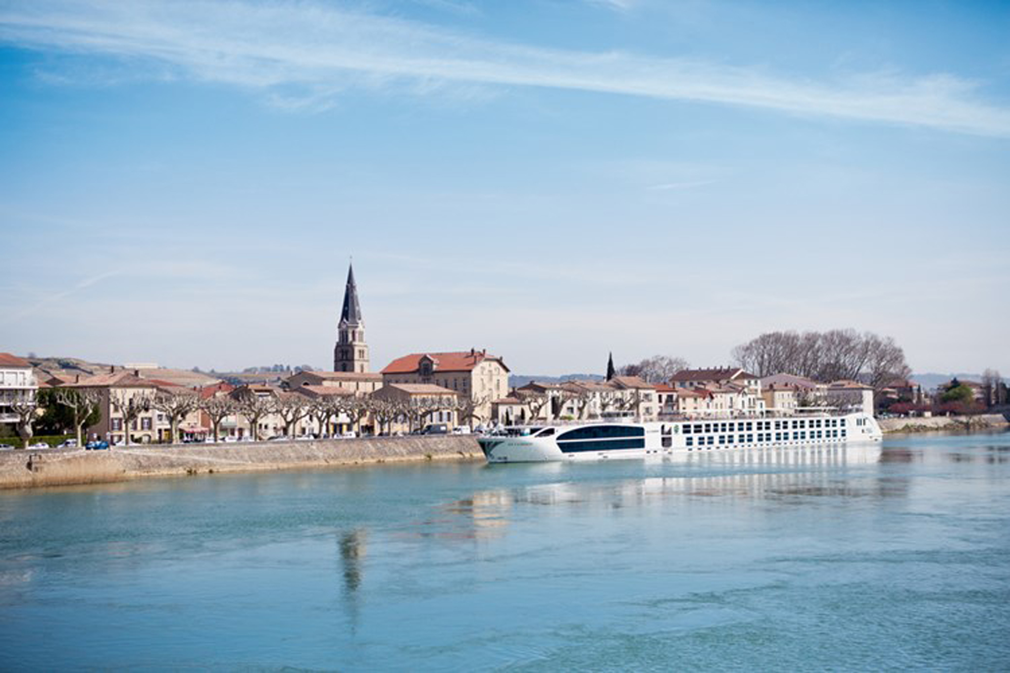 A modern white river cruise ship is moored along the waterfront of a charming European riverside