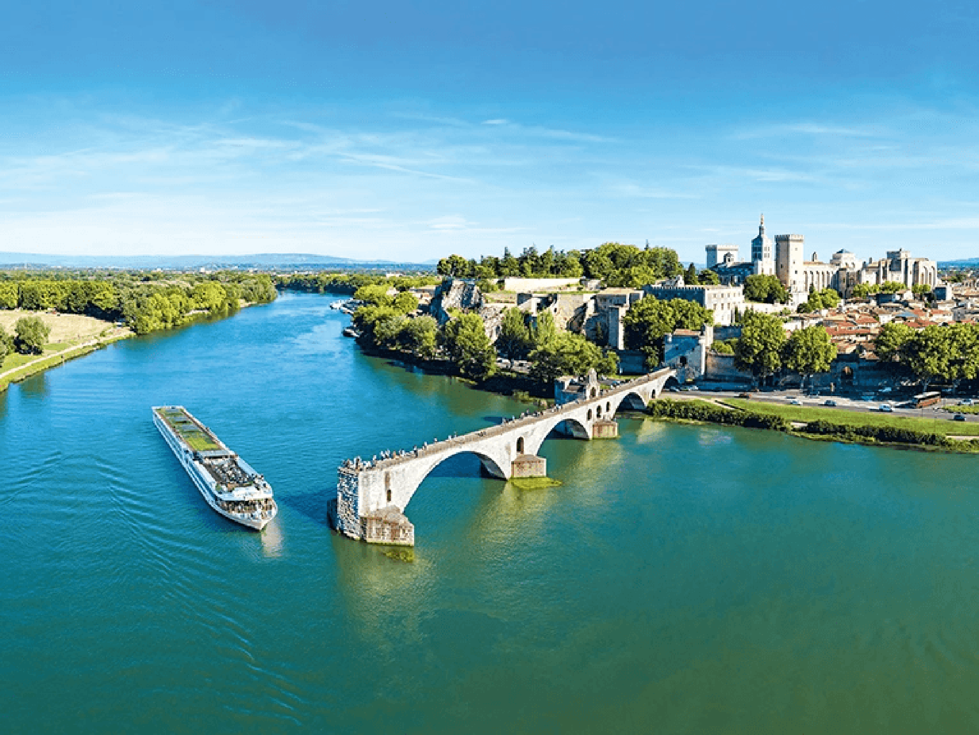 A scenic river cruise vessel navigates the Rhône River near the medieval walled city of Avignon