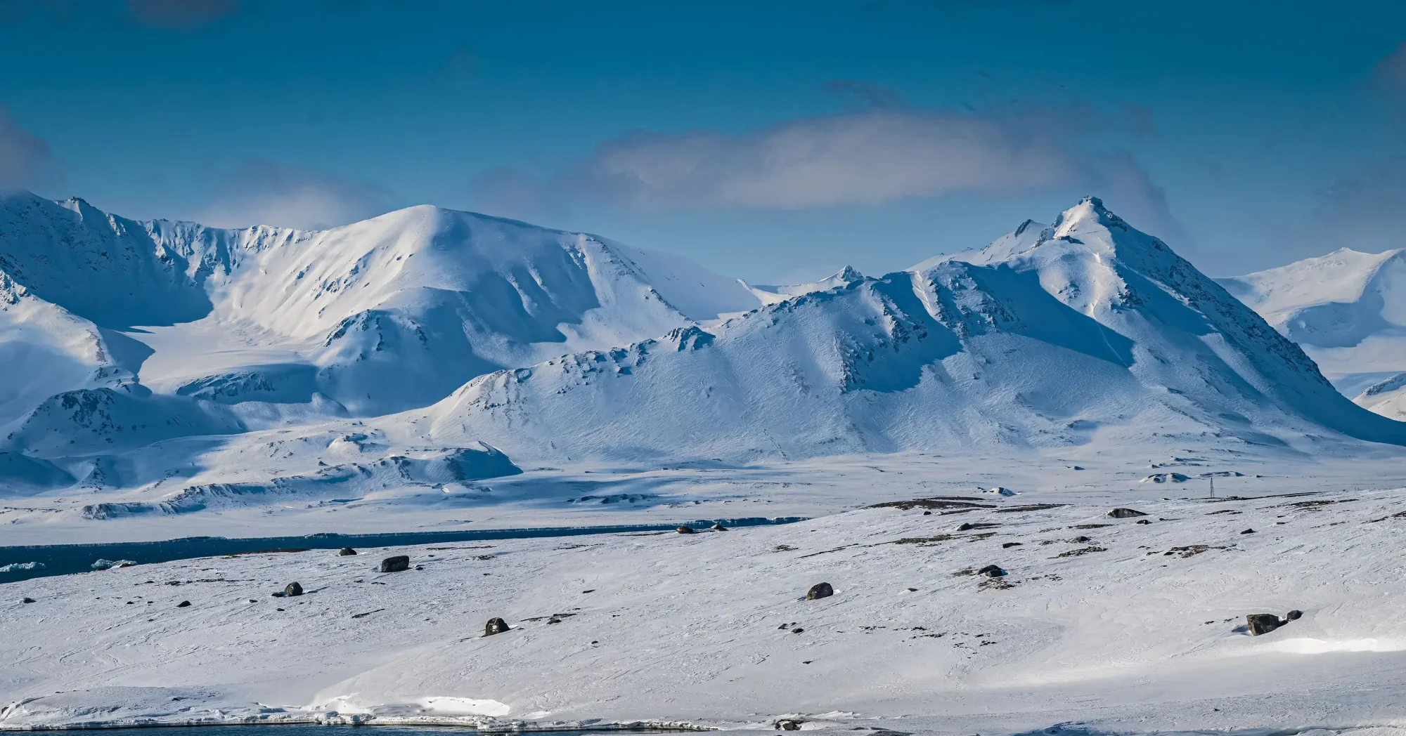 Snow-Covered Volcanic Mountains in Arctic A pristine Arctic landscape featuring multiple snow-covered volcanic peaks with distinct conical
