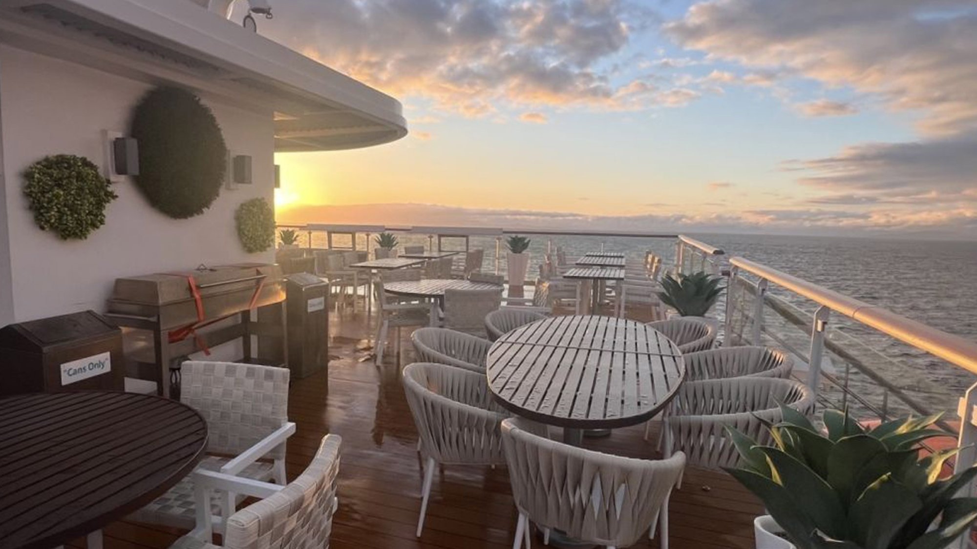 BBQ Deck at Sunset Aboard Ocean Victory An expansive outdoor BBQ deck on a cruise ship featuring multiple dining tables with comfortable