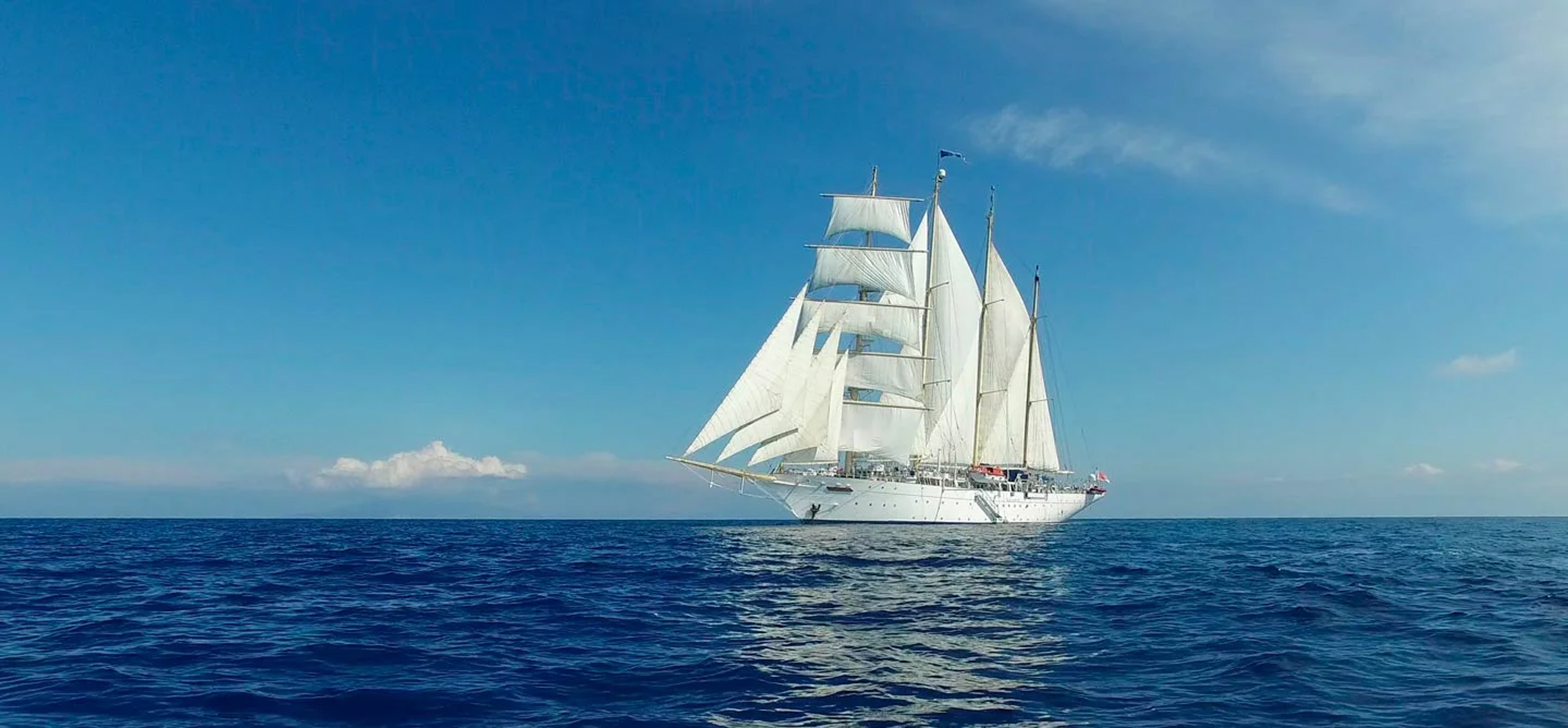 A stunning white-hulled tall ship with multiple masts and full canvas sails deployed, sailing