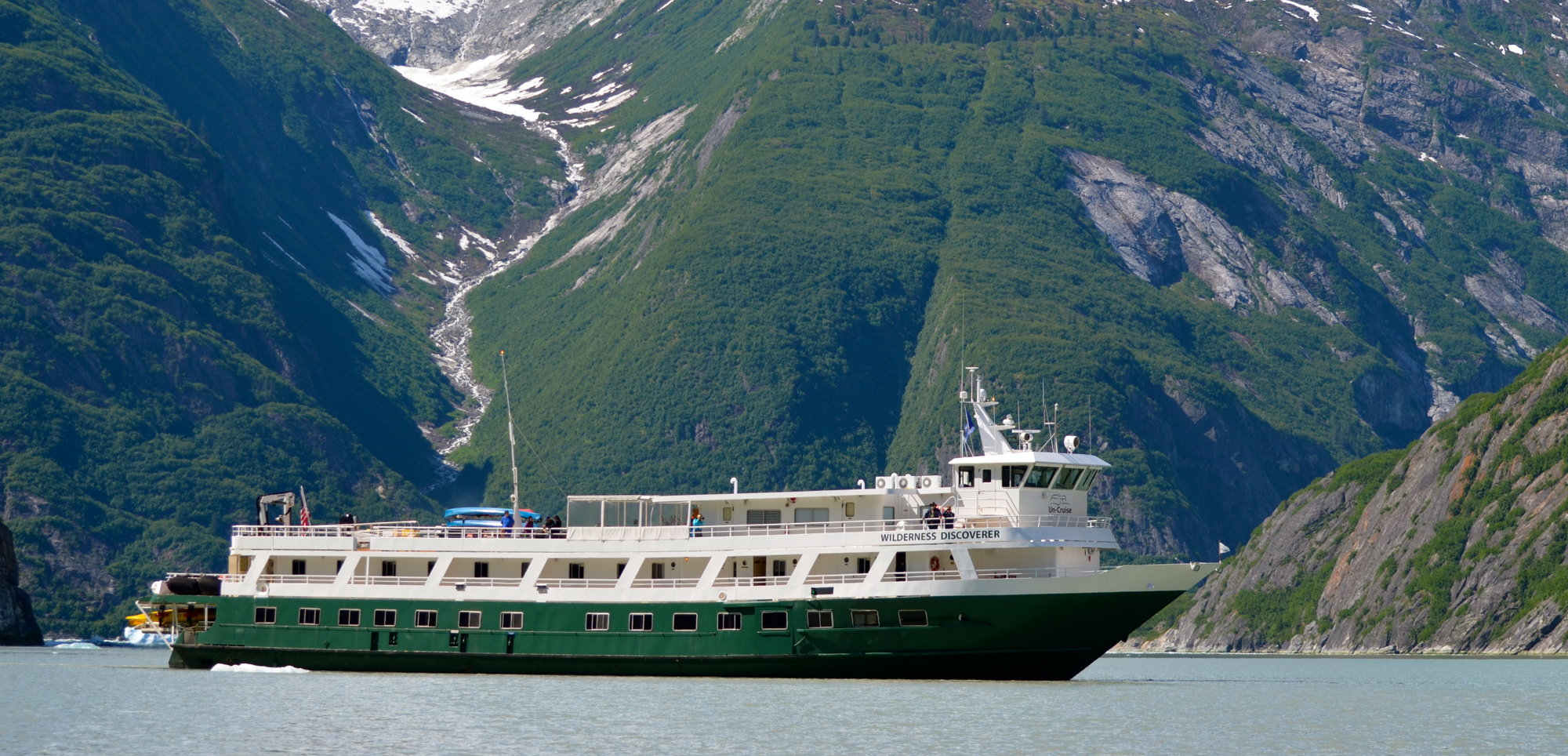 Wilderness Discoverer in Alaskan Fjords A green and white expedition cruise ship navigating through a stunning fjord with steep, forested