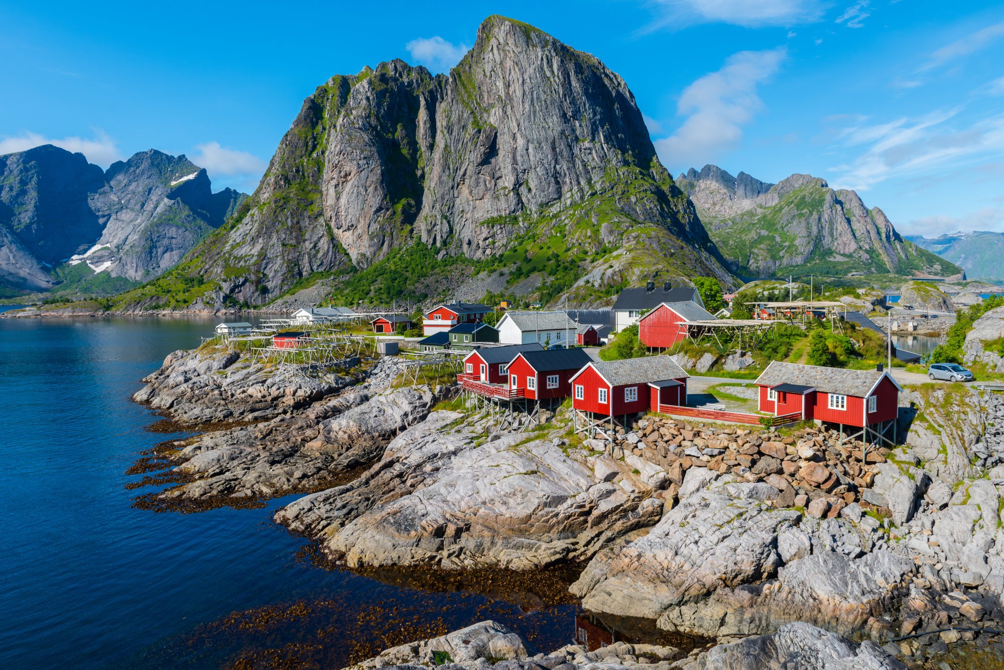 shutterstock_756604909 Scenic Norwegian fjord with steep green mountainsides, a small village nestled at the water's edge, and a cruise ship sailing through the calm deep blue waters.