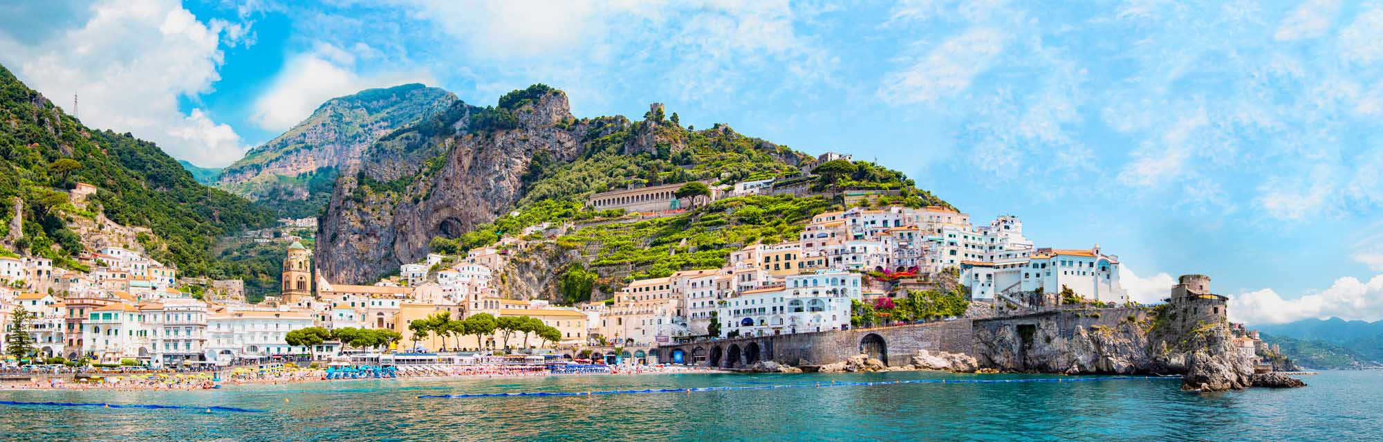 Amalfi Coast Village Coastal Panorama A stunning panoramic view of the picturesque Amalfi village nestled along dramatic cliffsides with colorful Mediterranean architecture, featuring pastel-colored houses cascading down the rocky coastline overlooking turquoise waters and a small sandy beach.