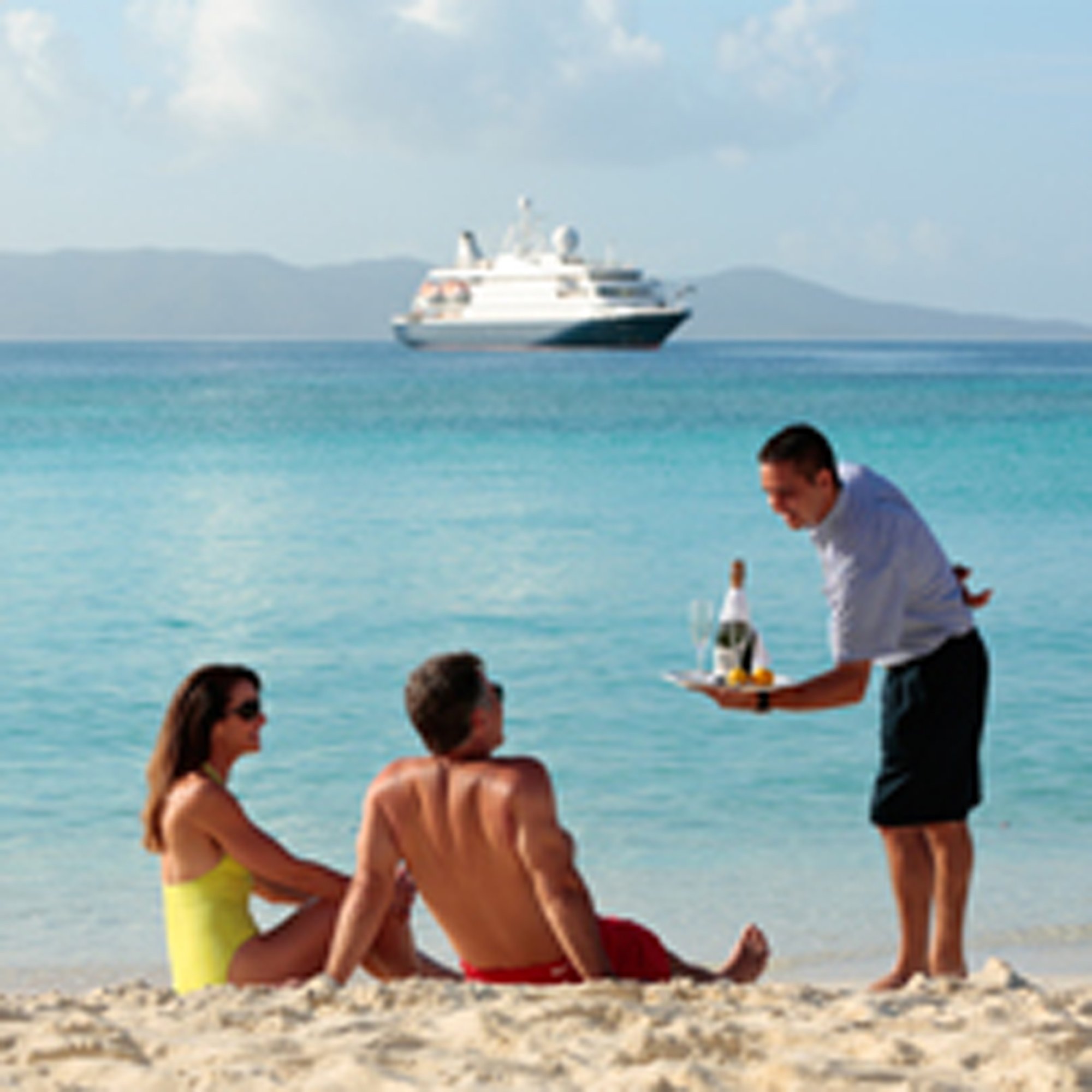 Beachside Service on Cruise Ship Excursion A male server in formal attire presents drinks and refreshments to two guests relaxing on