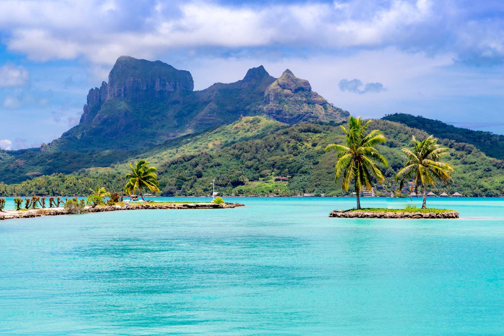 Bora Bora Island with Turquoise Lagoon A stunning tropical landscape featuring the distinctive volcanic peaks of Bora Bora rising dramatically from lush green slopes, framed by crystal-clear turquoise lagoon waters dotted with coconut palms and small islets in French Polynesia.