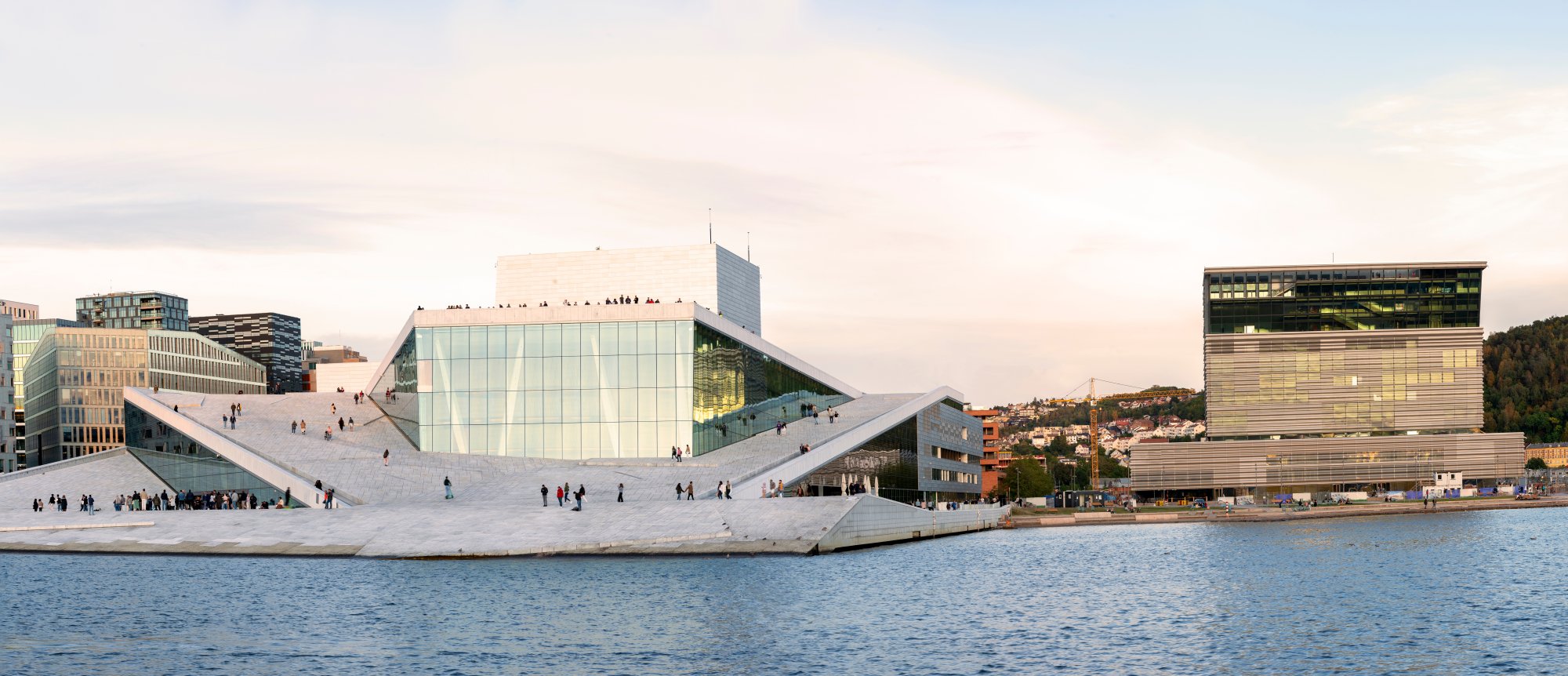 Copenhagen Opera House Waterfront Architecture The striking modern Copenhagen Opera House dominates the waterfront with its distinctive white marble sloped architecture and glass facade, flanked by contemporary buildings and reflecting in the calm harbor waters. The iconic cultural landmark showcases Scandinavian design excellence with its bold geometric forms and public plaza.