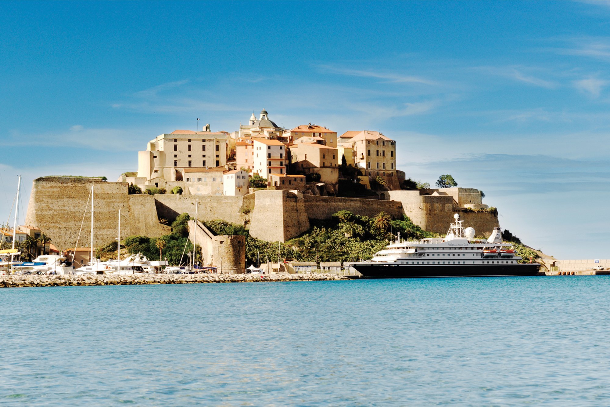 Citadel of Corte with Cruise Ship in Harbor A picturesque medieval citadel perched on a rocky promontory overlooking a turquoise Mediterranean
