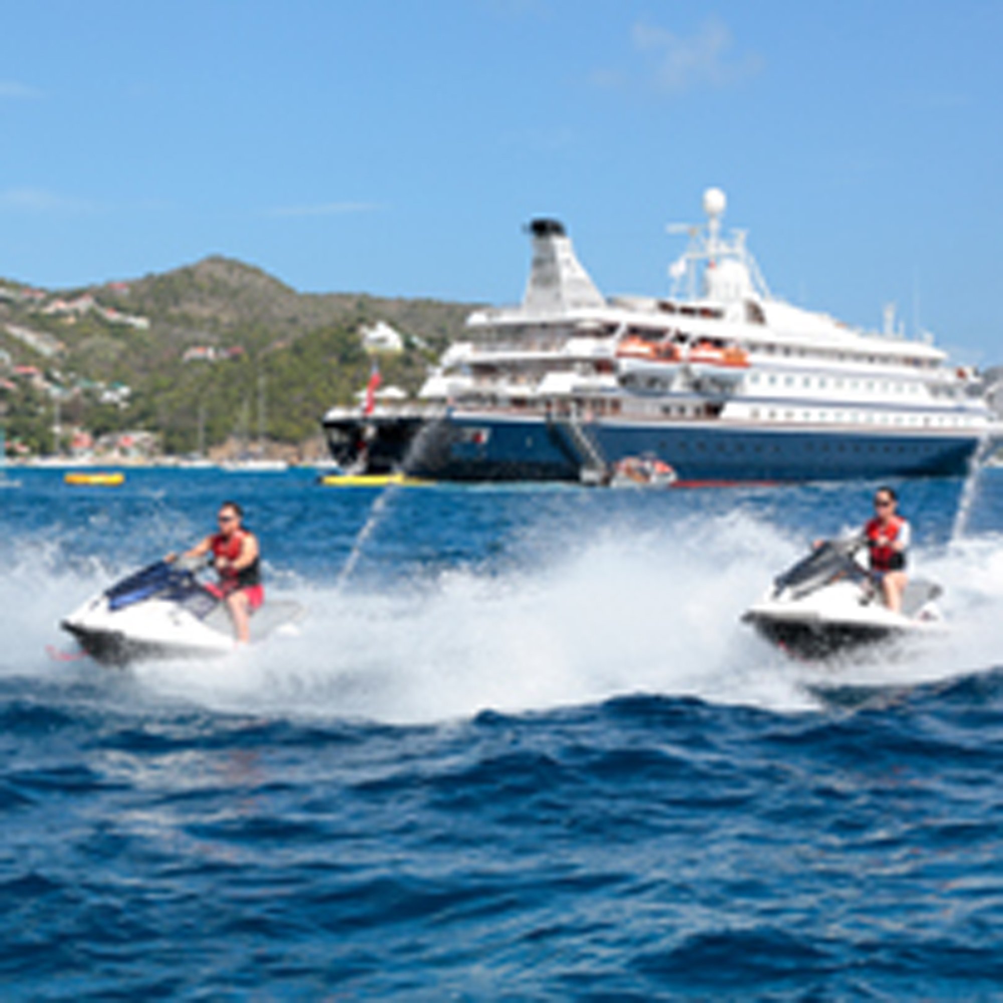 Jet Ski Adventure Near Cruise Ship Two passengers enjoy jet skiing in crystal-clear blue waters with a large white and blue cruise