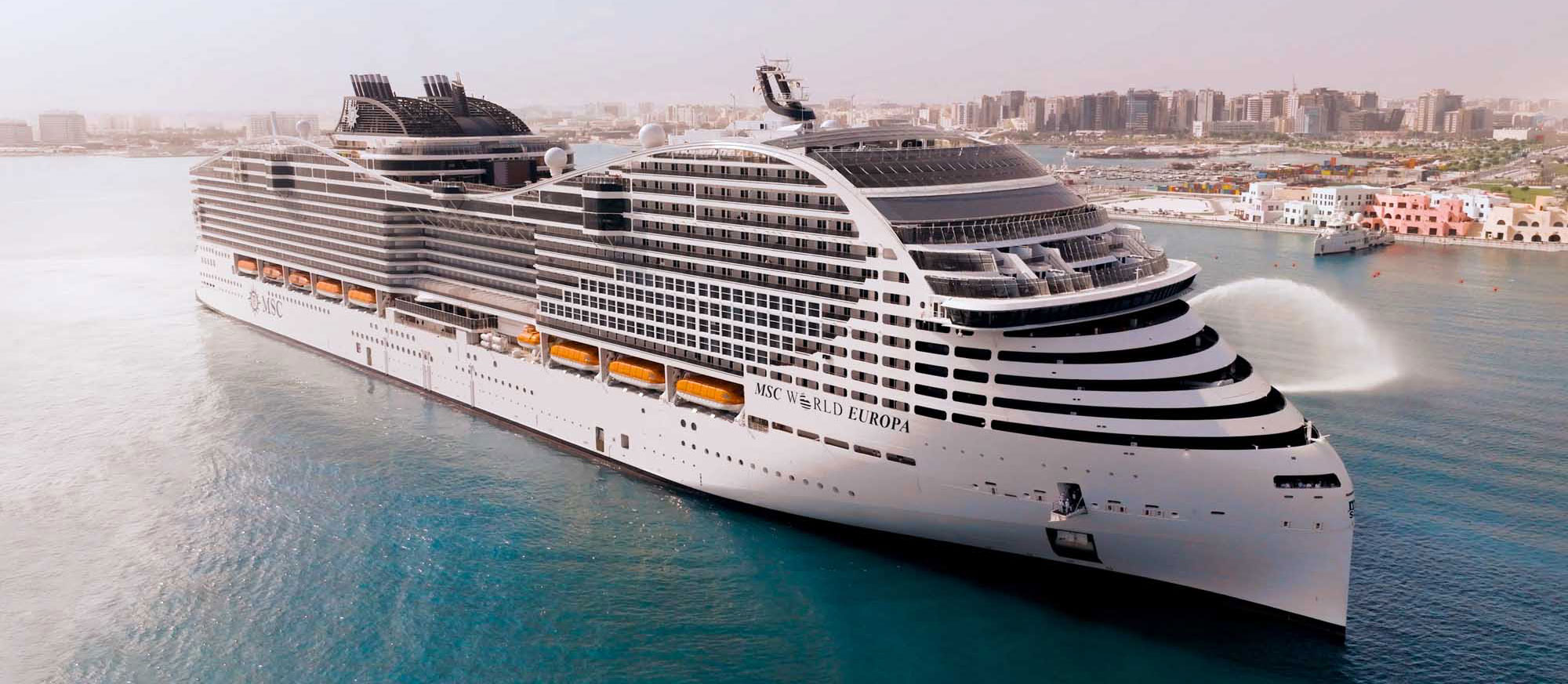 MSC World Europa Cruise Ship at Port A magnificent modern cruise ship, the MSC World Europa, docked in a turquoise Mediterranean port with a coastal cityscape visible in the background. The vessel showcases distinctive contemporary design with tiered black and white balconies, multiple decks, and modern amenities characteristic of next-generation cruise ships.