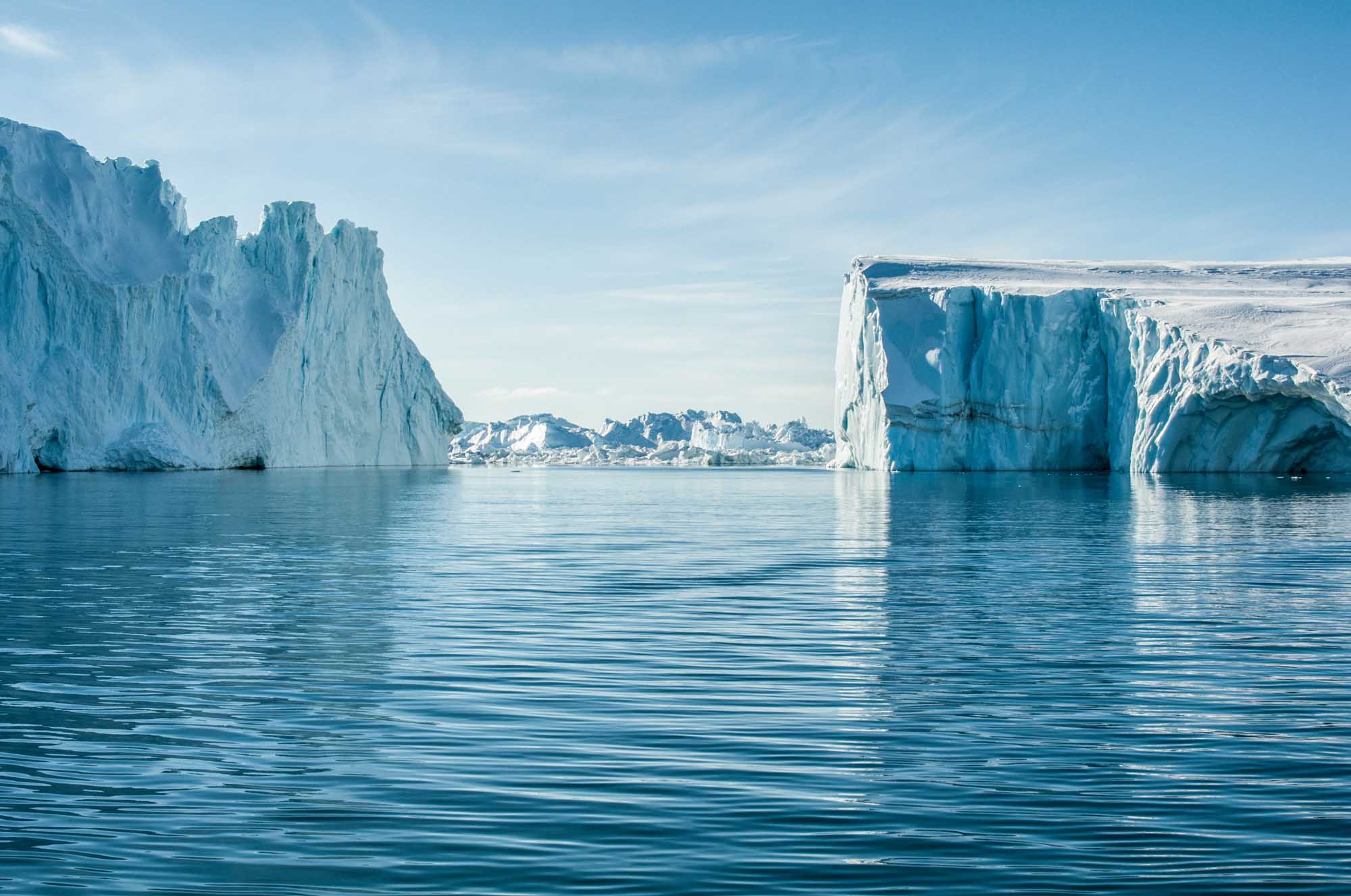Majestic Icebergs in Greenlandic Waters Towering white and blue icebergs float in calm turquoise Arctic waters, with a small Greenlandic