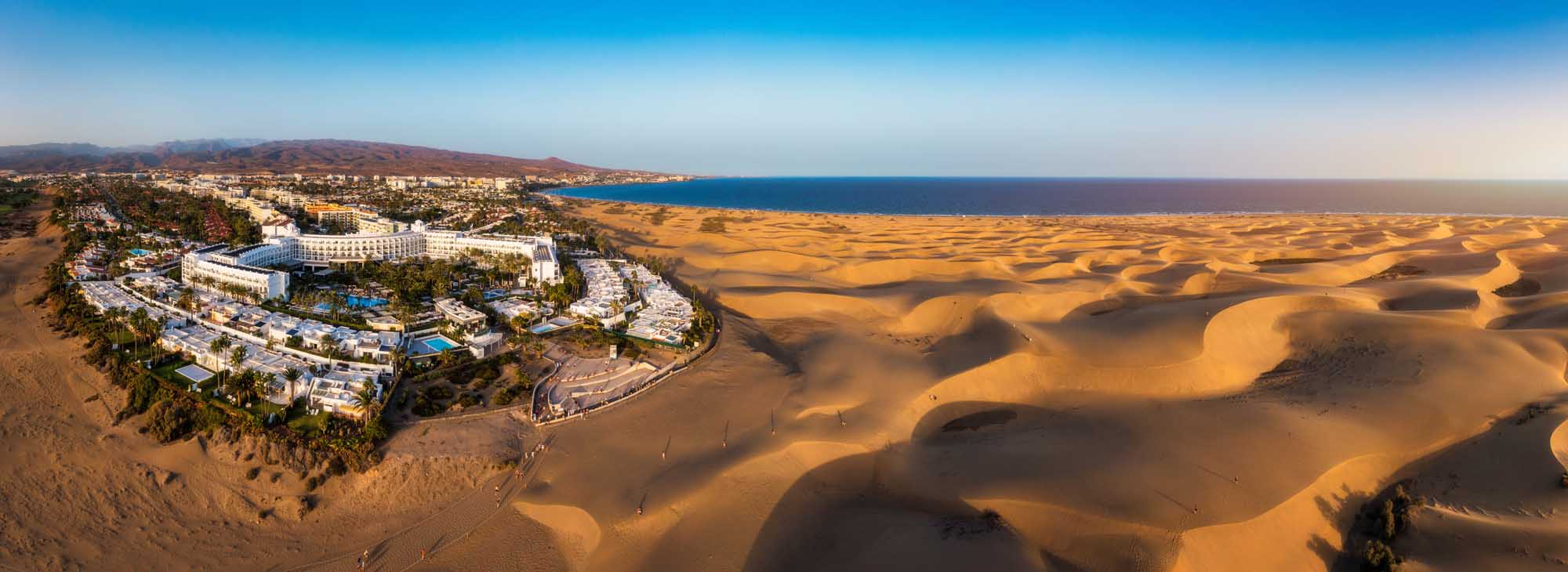 Maspalomas Dunes and Resort, Gran Canaria An aerial view of the golden sand dunes of Maspalomas Natural Reserve in Gran Canaria, with a luxurious beachfront resort nestled on the coast overlooking the Atlantic Ocean and surrounding desert landscape.