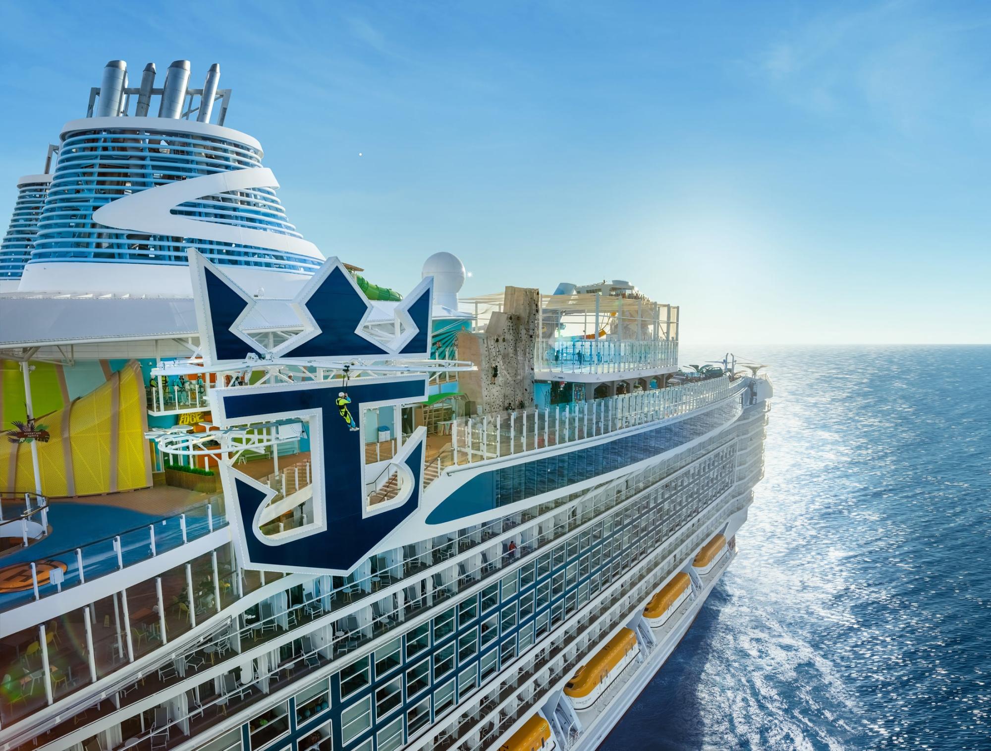 Modern Cruise Ship at Sea with Anchor Emblem A modern cruise ship with distinctive blue and white livery featuring a large anchor emblem on its hull, photographed from the side while at sea. The ship displays multiple decks with balconies, colorful amenities including yellow waterslides, and multiple smokestack funnels, representing contemporary cruise industry design and luxury ocean travel.