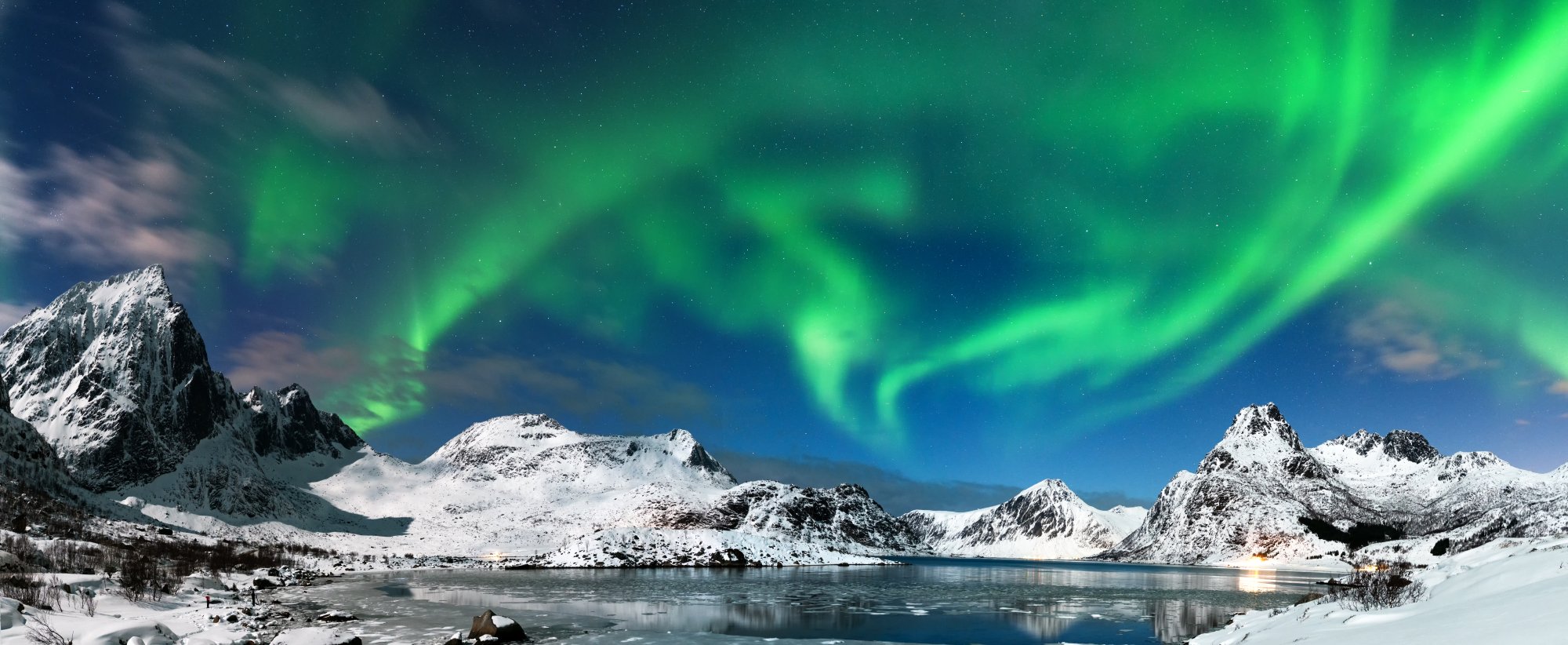 Northern Lights Over Snow-Capped Mountain Lake A breathtaking Arctic landscape featuring vibrant green aurora borealis dancing across the night sky above a serene frozen fjord, surrounded by majestic snow-covered peaks and dark rocky outcrops. The ethereal light display reflects on the calm water below, creating a stunning natural spectacle characteristic of polar regions.
