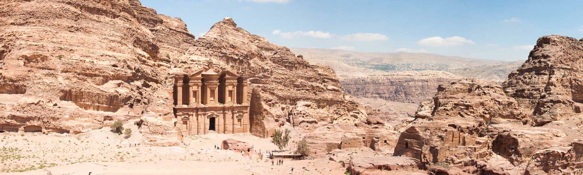 Petra’s Monastery carved into desert rock An iconic view of Al-Deir (The Monastery), one of Petra's most magnificent rock-carved facades, featuring grand Nabatean columns and architectural details set within towering sandstone cliffs in the Jordanian desert. The massive structure stands as a testament to ancient engineering carved directly from the russet and tan stone formations.