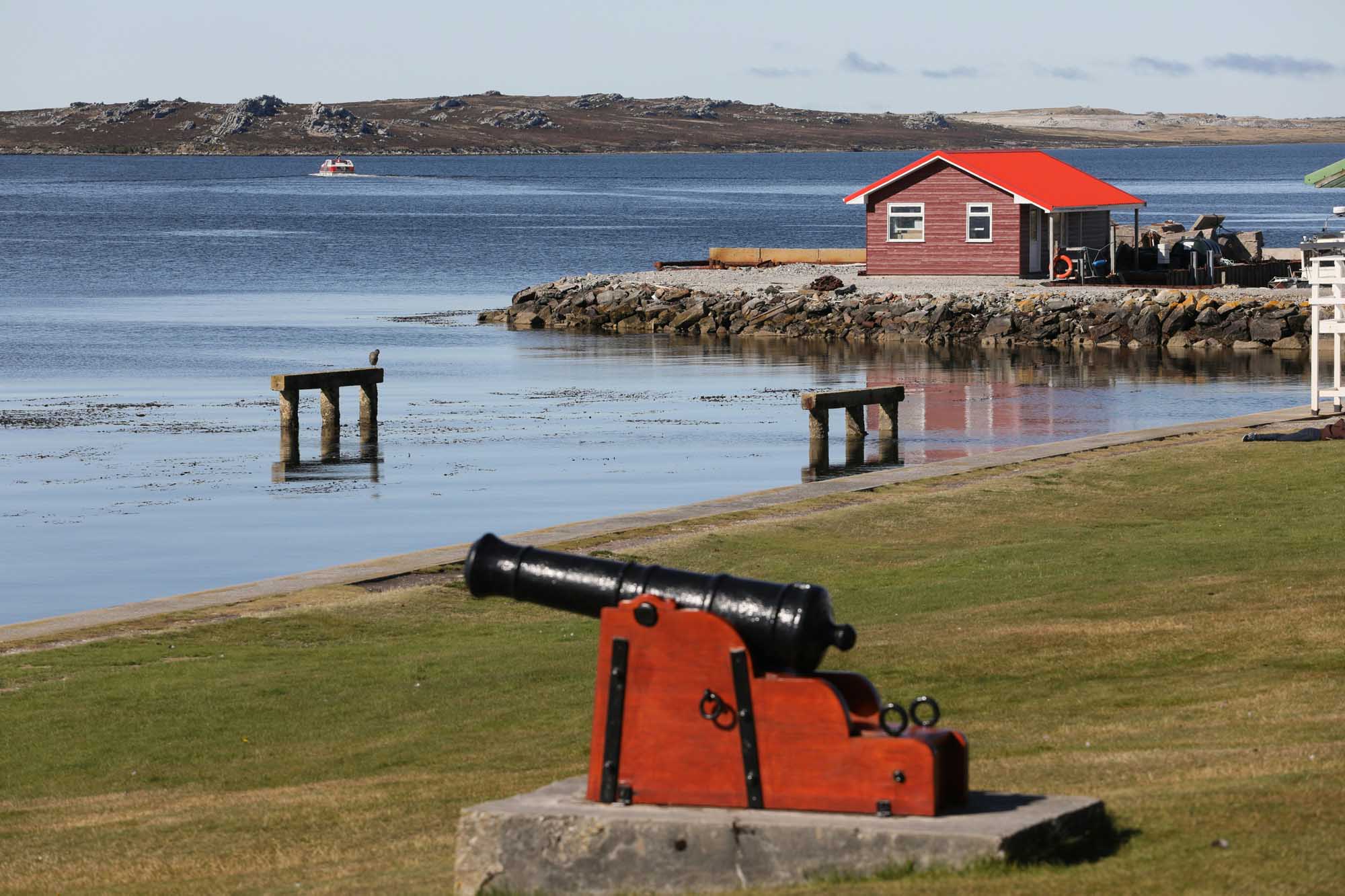 Red Boathouse and Cannon on Arctic Coastline A picturesque Arctic coastal settlement featuring a distinctive red-roofed boathouse perched on