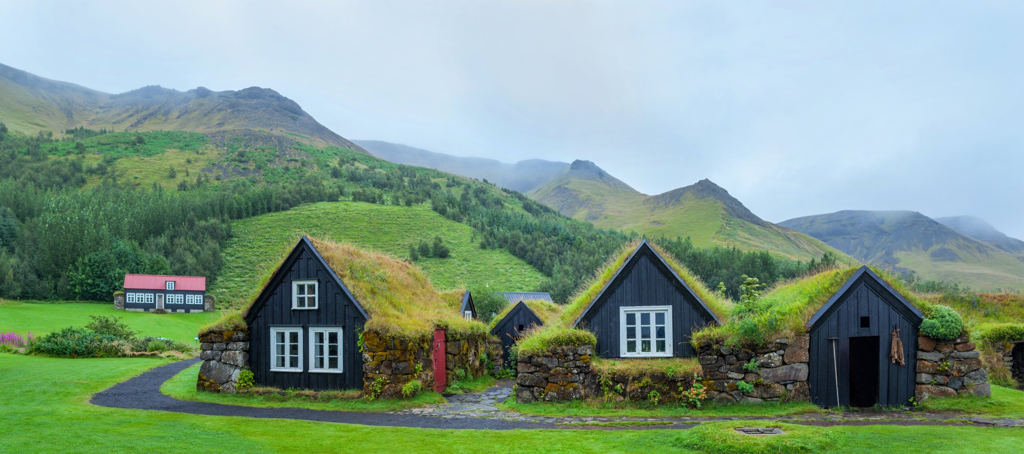 Traditional Icelandic Turf-Roofed Houses in Mountain Valley A picturesque cluster of traditional Icelandic turf-roofed houses with distinctive black wooden