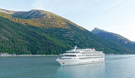 A mid-sized cruise ship operated by American Cruise Lines navigates pristine turquoise waters