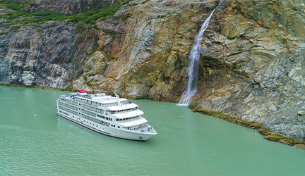 A modern small cruise ship operated by American Cruise Lines navigates striking turquoise glacial