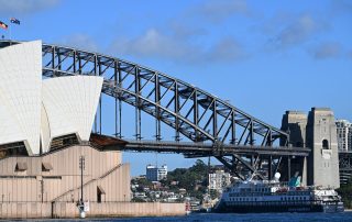 Aurora Expeditions Ship at Sydney Harbour Bridge A blue expedition cruise ship from Aurora Expeditions passes beneath the iconic Sydney Harbour