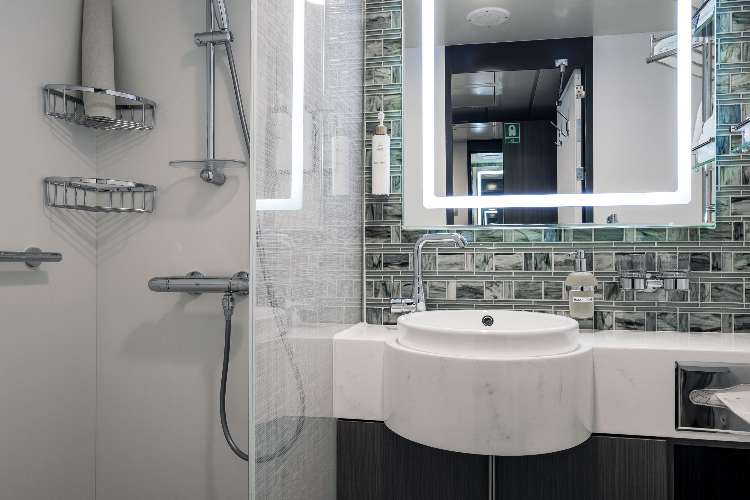 Aurora Stateroom Superior Bathroom A modern cruise ship stateroom bathroom featuring a curved white marble vessel sink, illuminated