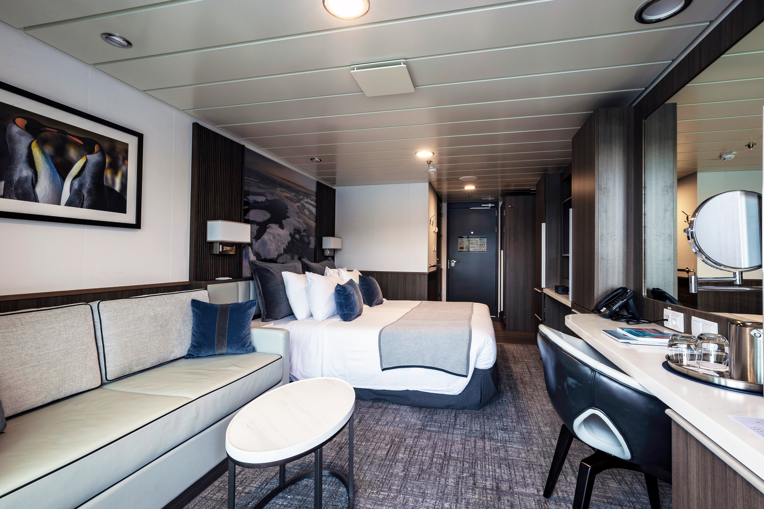 Aurora Stateroom Superior with Elegant Modern Design A luxurious cruise ship stateroom featuring a king bed with white linens and blue accents