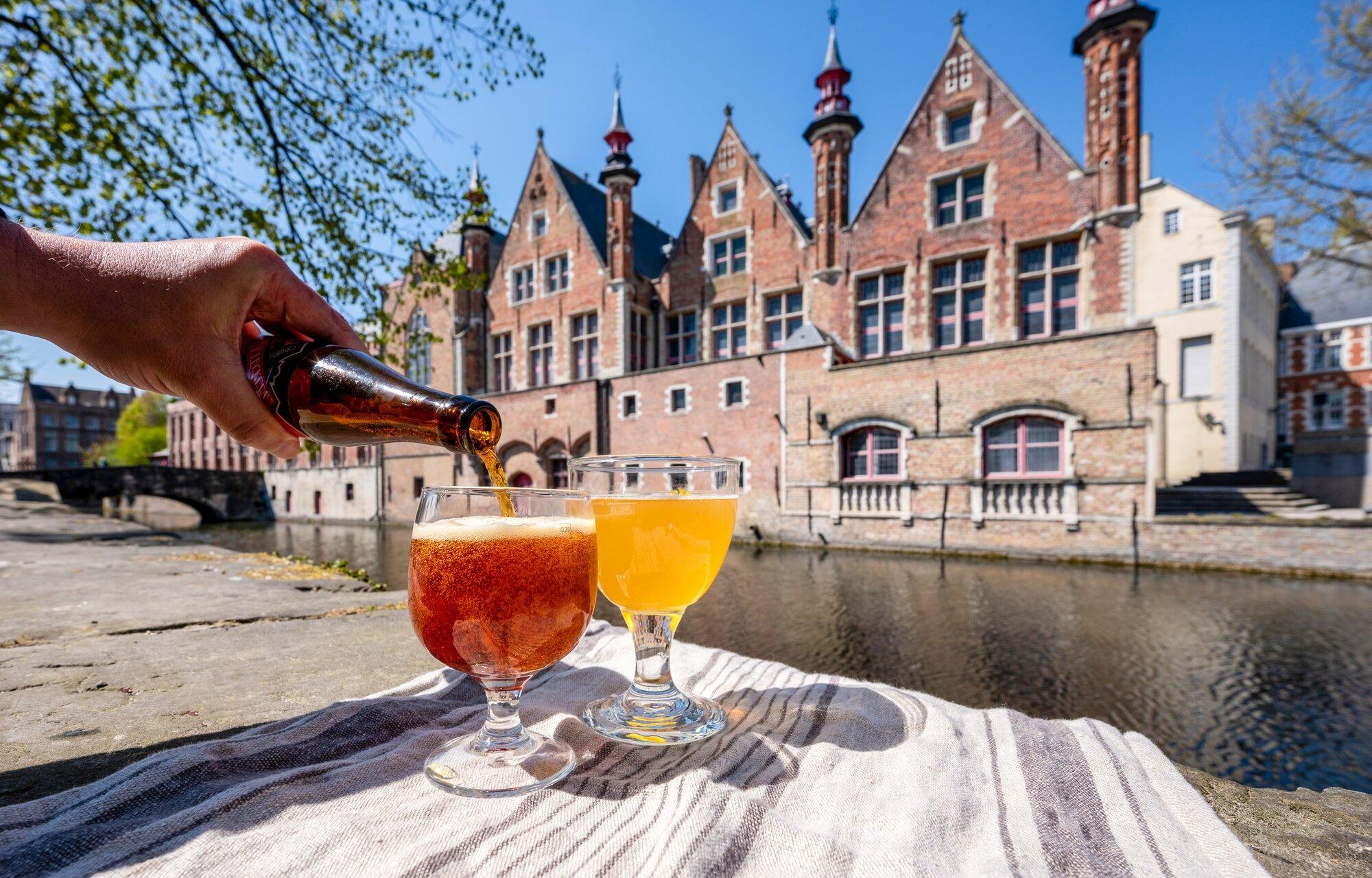 Belgian Beer Pour in Historic Bruges A hand pours amber beer from a bottle into two glasses on the waterfront of Bruges, Belgium