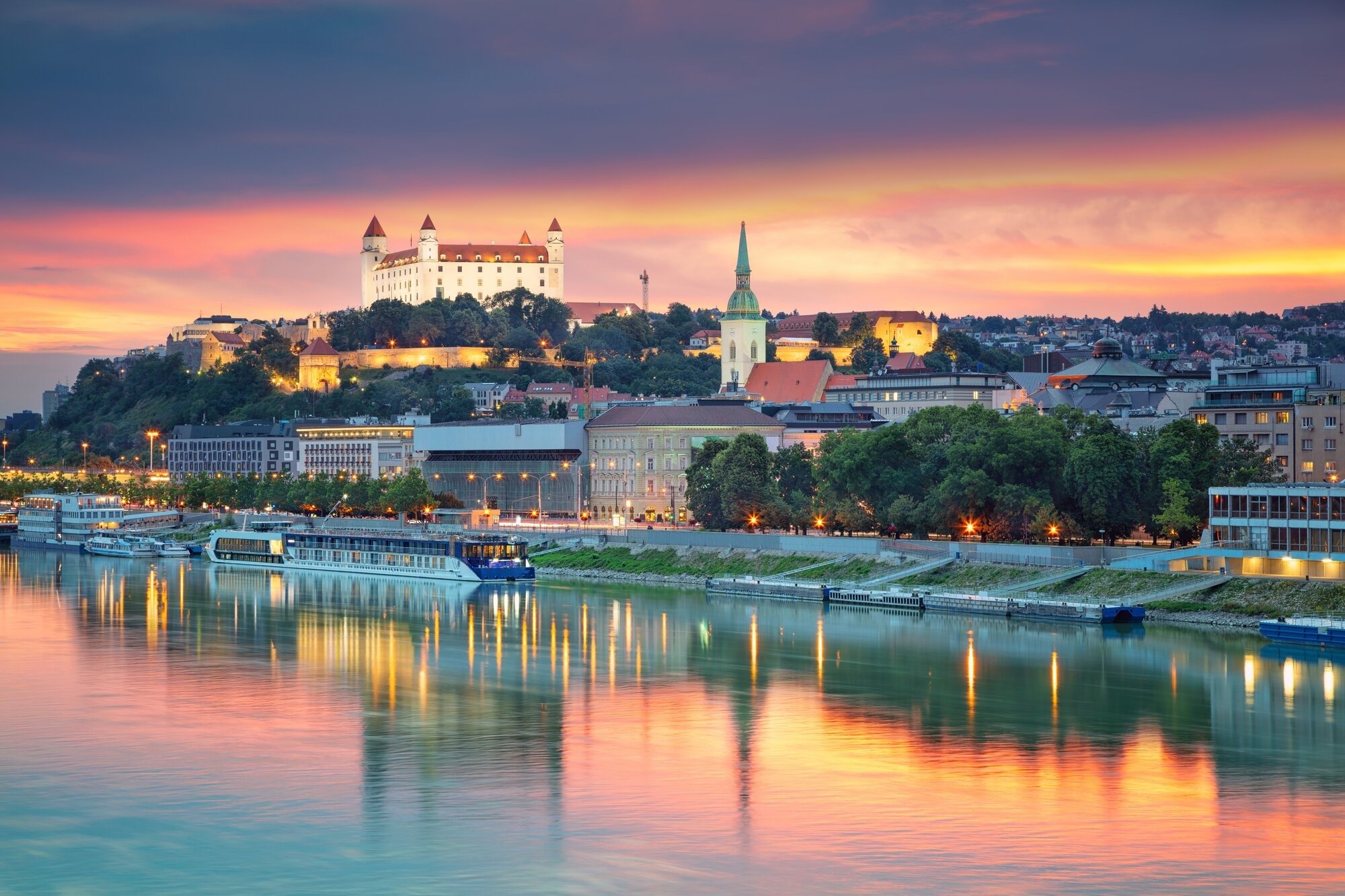 Bratislava Castle at Sunset Over the Danube River A stunning twilight view of Bratislava, Slovakia, featuring the iconic hilltop castle illuminated