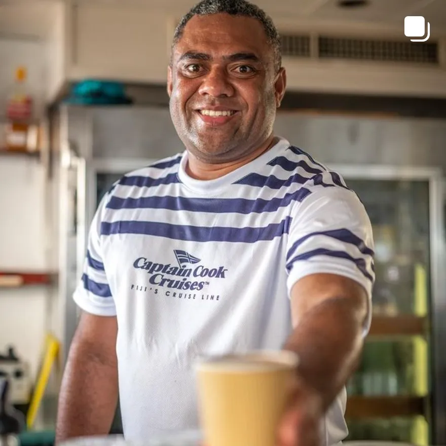 Captain Cook Cruises Fiji Staff Member A smiling male staff member wearing a Captain Cook Cruises branded striped t-shirt, holding a glass